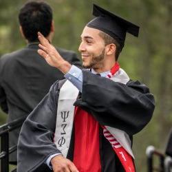 Image of a Justice Studies student waving to the crowd and wearing a cap and gown at a convocation ceremony.