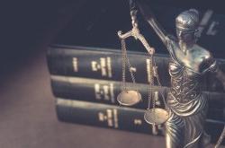 Image of law books in the background with a small scales of justice statue in the foreground.