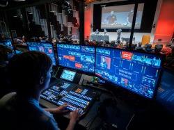 A student in front of several TV production monitors, controlling audio and visual elements of a show.